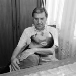 Screenshot An elderly man lovingly holding a young child on his lap indoors.