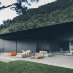 Modern outdoor seating area with gray sofas and orange cushions against a mountain backdrop.
