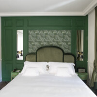Hotel La Gemma in Florence Elegant bedroom with green accents and patterned wallpaper behind a plush bed.