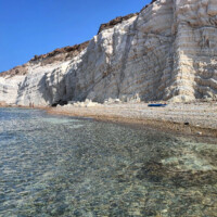 Clear water meets towering white cliffs under a bright blue sky.