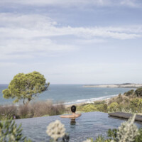 Person relaxing in an infinity pool overlooking the ocean and coastline.