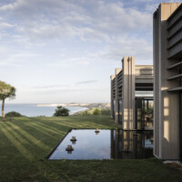 ©AlexFilz . Adler Sicily 2022 Modern building with reflective pool overlooking ocean at sunset.