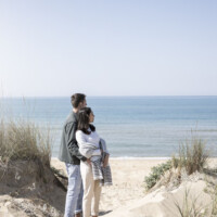 Couple embracing on a sandy beach with calm ocean in the background.