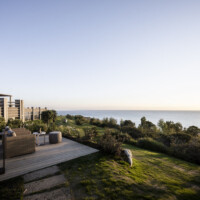 Couple enjoying a scenic coastal view from a grassy terrace at sunset.