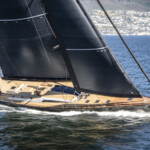 Sleek sailboat with black sails gliding over water.