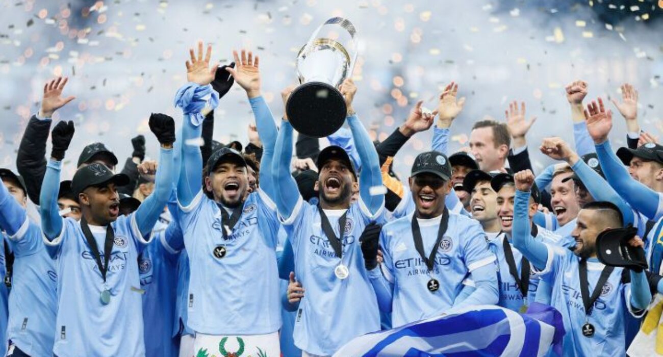 Manchester City players celebrate winning a trophy with champagne.