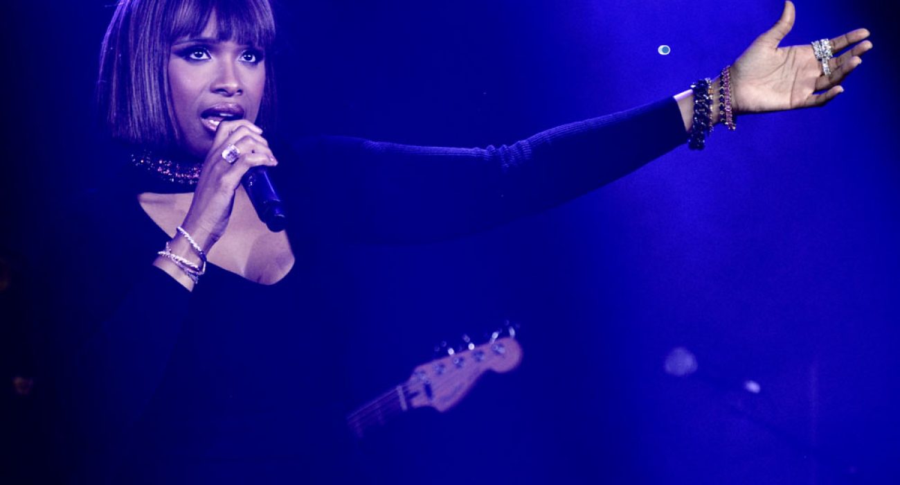 Female singer performing on stage with a microphone under blue lighting.
