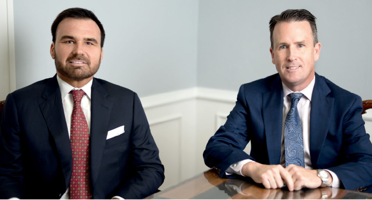 Two men in suits seated at a table in a professional setting.