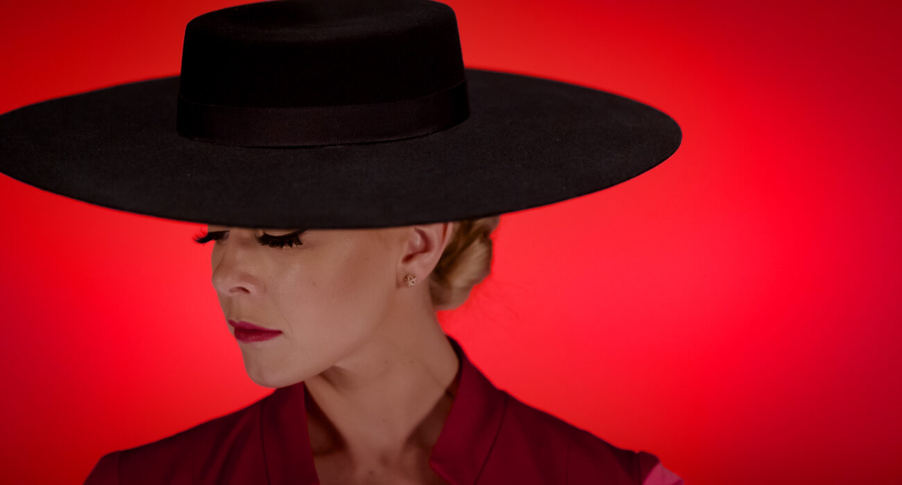 Woman wearing a wide-brimmed black hat against a red background.