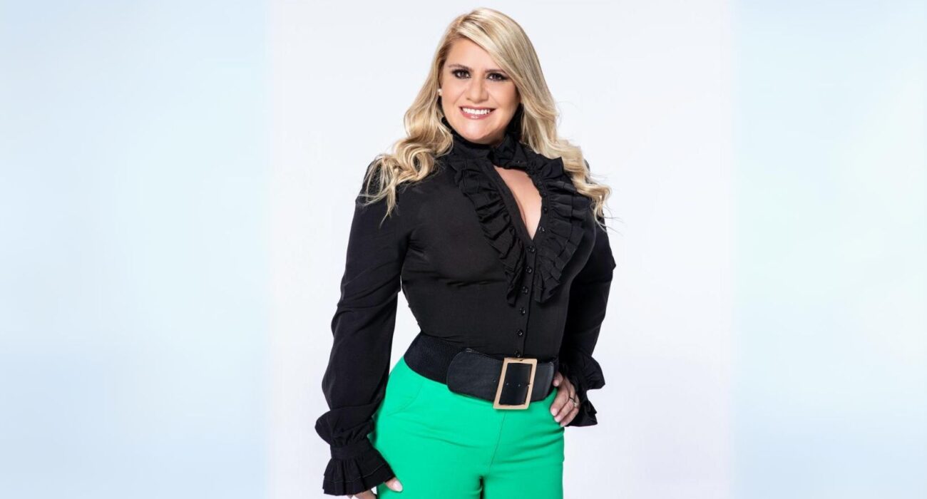 Smiling woman in a black ruffled blouse and green pants.