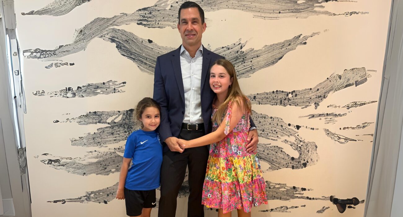 Man posing with two young girls in front of a textured wall.