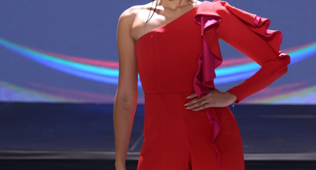 Model in a striking red one-shoulder jumpsuit on runway.