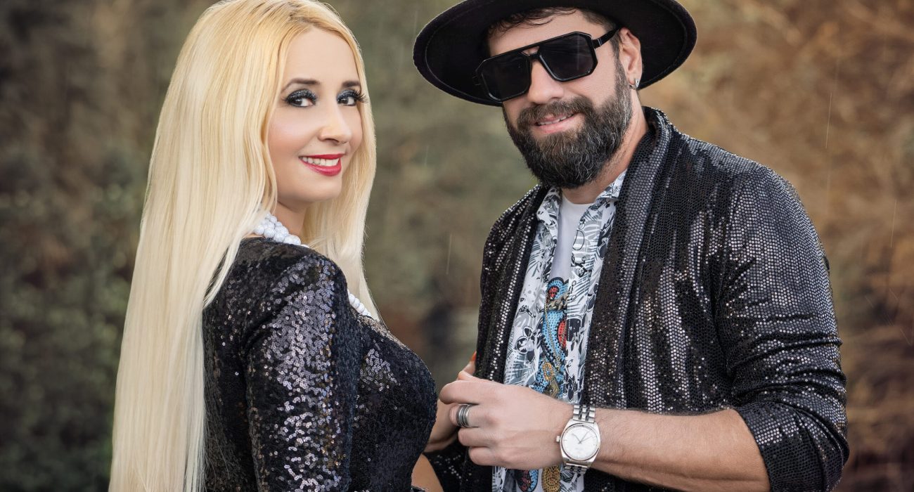 A stylish couple poses outdoors, both wearing dark velvet jackets.
