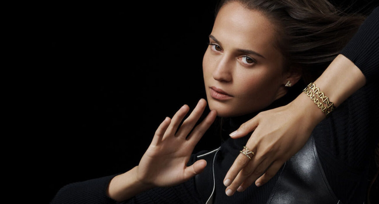 Serious woman with focused expression, hands raised defensively against a black background.