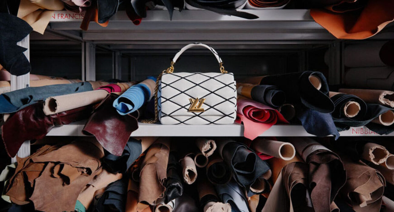 Elegant white handbag with gold accents displayed among rolled fabrics.