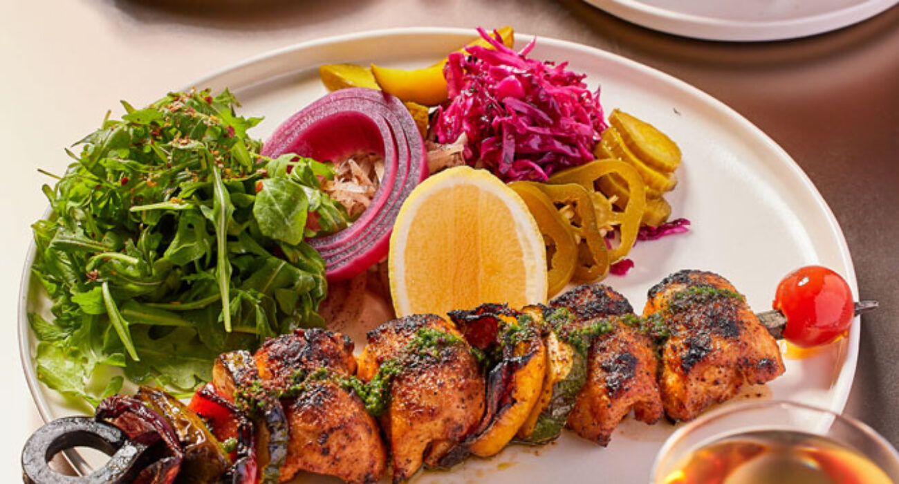 Grilled vegetable skewers served with fresh greens and lemon.