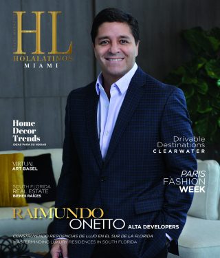 Retrato de un hombre sonriente de traje, con un fondo de hojas verdes.