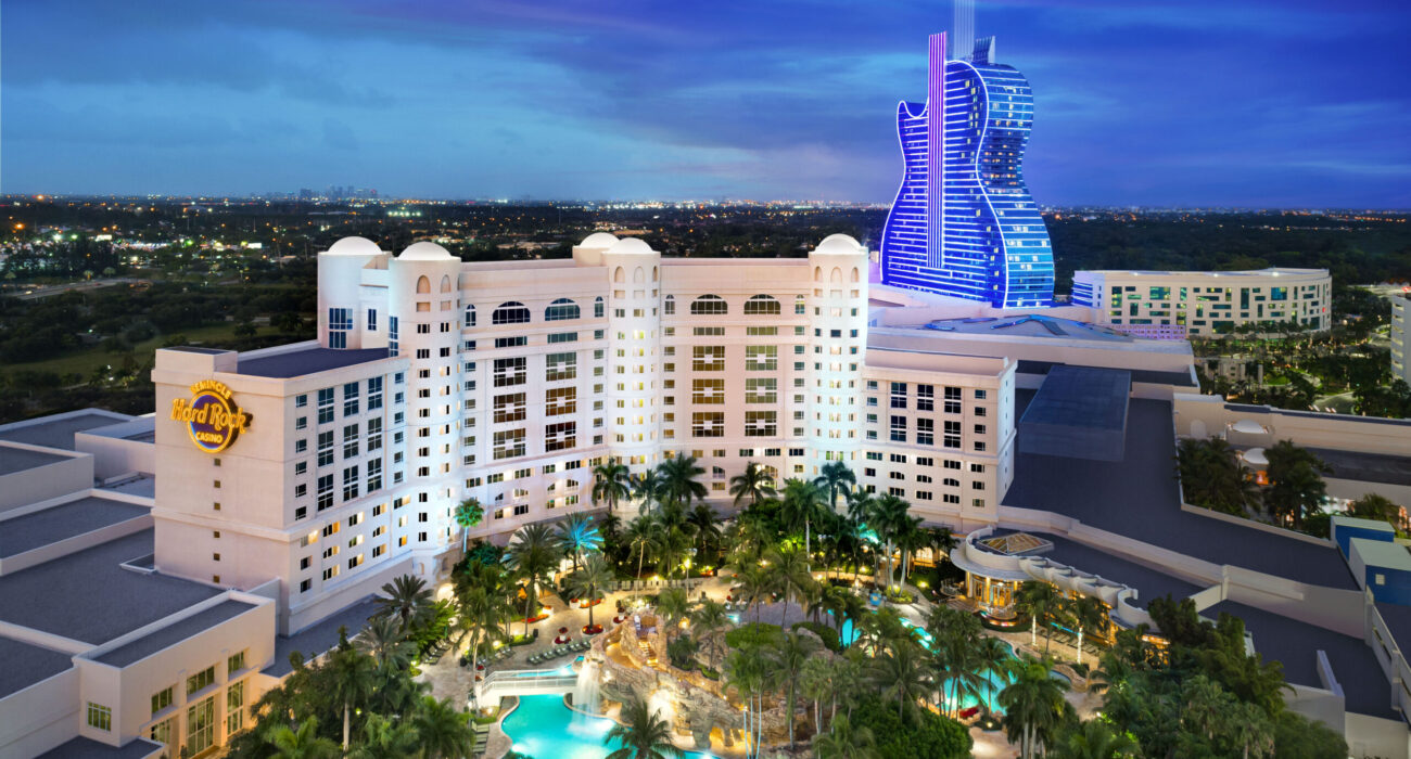 Luxurious hotel with illuminated pool and unique guitar-shaped building at night.
