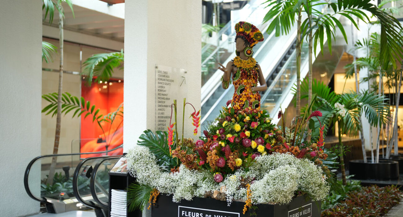 Floral sculpture of a woman made from colorful flowers in a public space.
