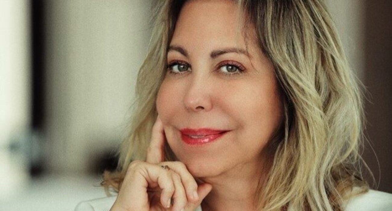 Smiling woman with light hair resting her chin on her hand.