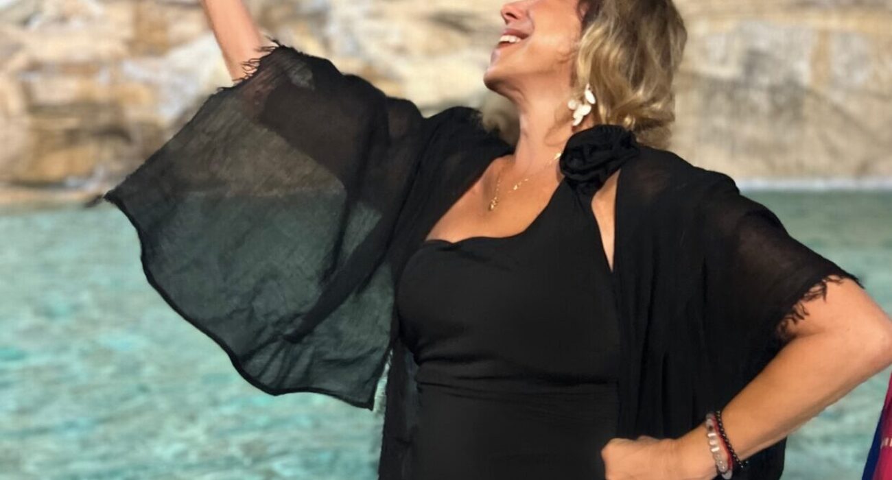 Woman in black dress joyfully posing by a fountain.