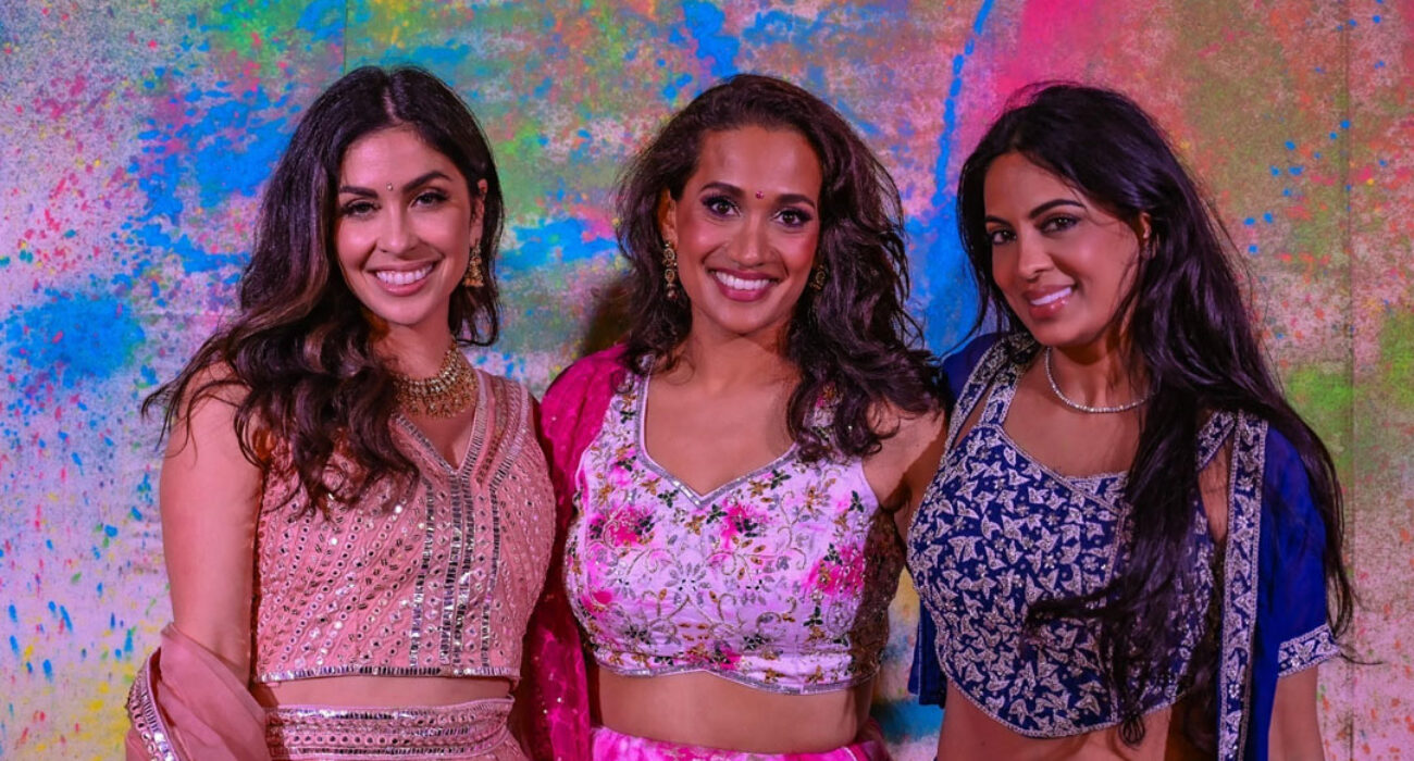 Three smiling women in colorful, festive attire against a vibrant backdrop.